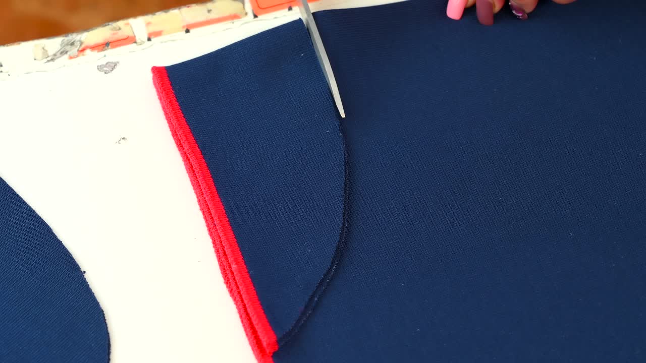 Woman hands cutting a blue knitted fabric with scissors in an workshop. Overhead shot. Close up