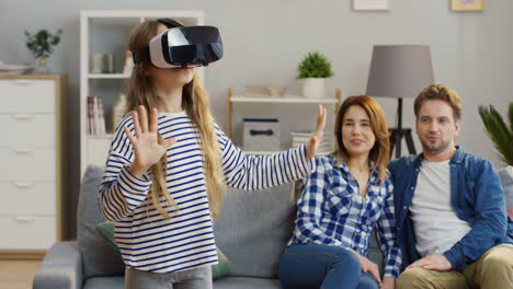 pequeña y linda chica rubia con gafas vr que tiene un auricular vr en la sala de estar