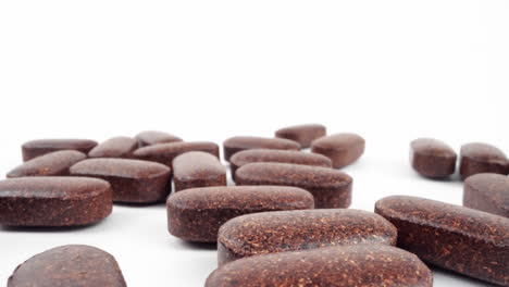 high-key shot of natural brown herbal pills spread on a bright white background