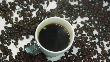 taza de café caliente blanca con vapor, rodeada de granos de café tostados, girando sobre un plato giratorio