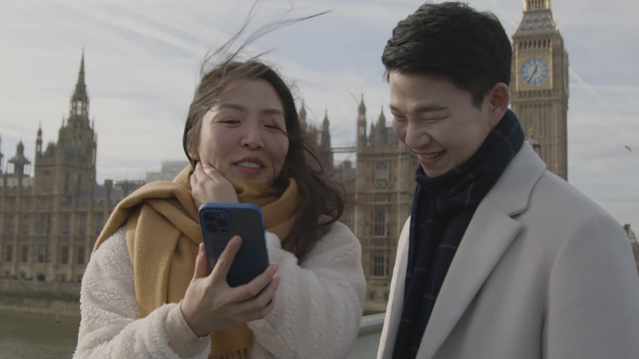 joven pareja asiática de vacaciones posando para selfie frente a las casas del parlamento en londres, reino unido 2