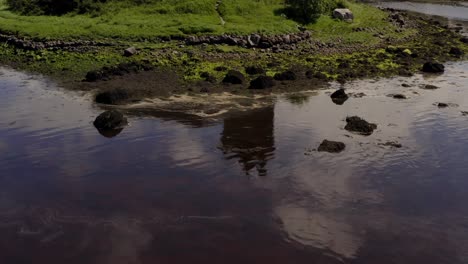 Dynamische-Luftaufnahme-Scannt-Dunguaire-Castle-Von-Einer-Reflexion-Auf-Dem-Wasser-Zu-Seiner-Wirklichen-Spitze