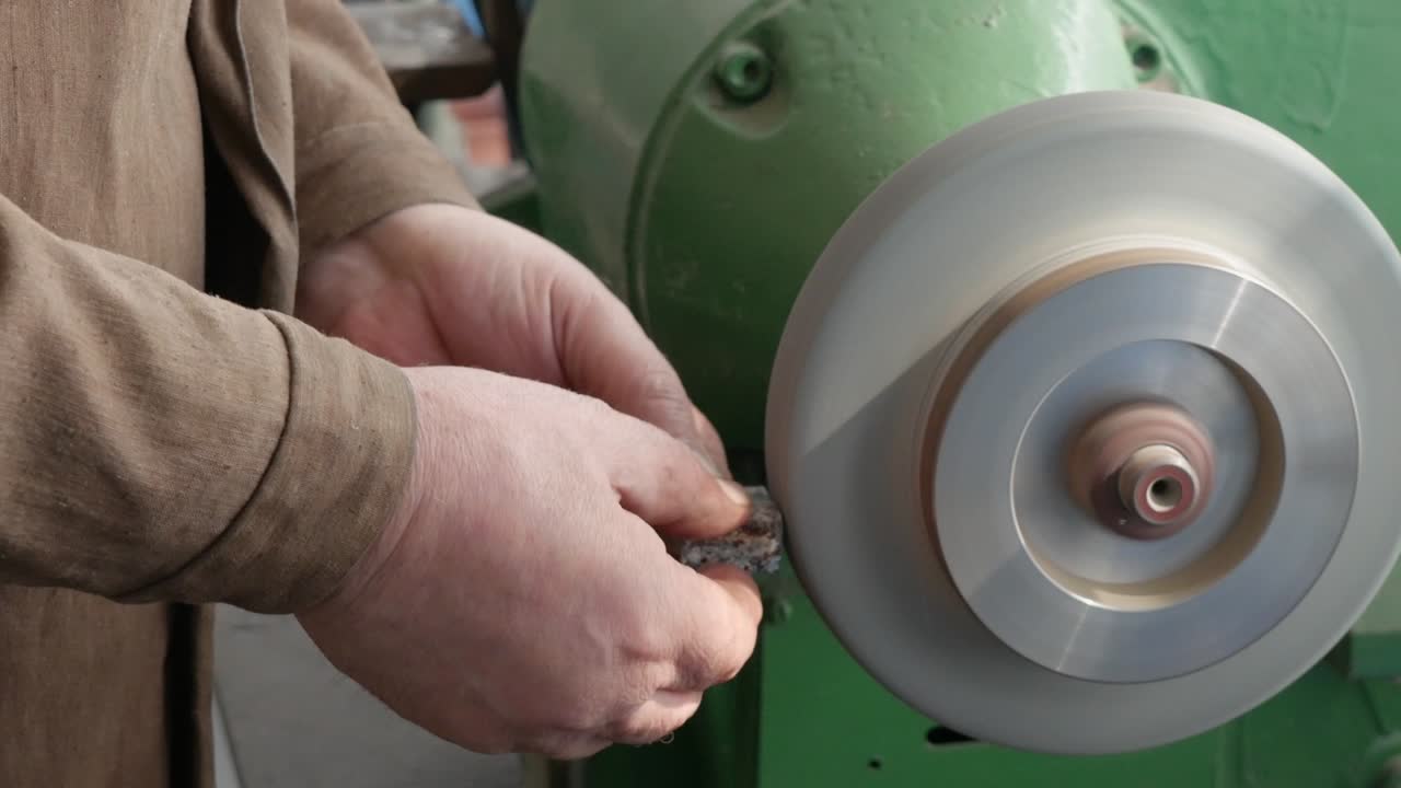 старые руки мастер шлифовать деталь на скамейке шлифовальной машины, грубая шлифовочная машина, крупный план. работа на пьедестальном шлифователе, производство предметов. финиш-шлифовальная металлическая часть на заводе