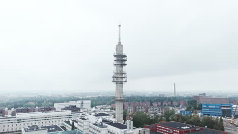 Aerial-wide-shot-of-a-bleak-industrial-concrete-television-and-radio-link-tower-in-Pasila,-Helsinki,-Finland-on-a-bright-and-foggy-day