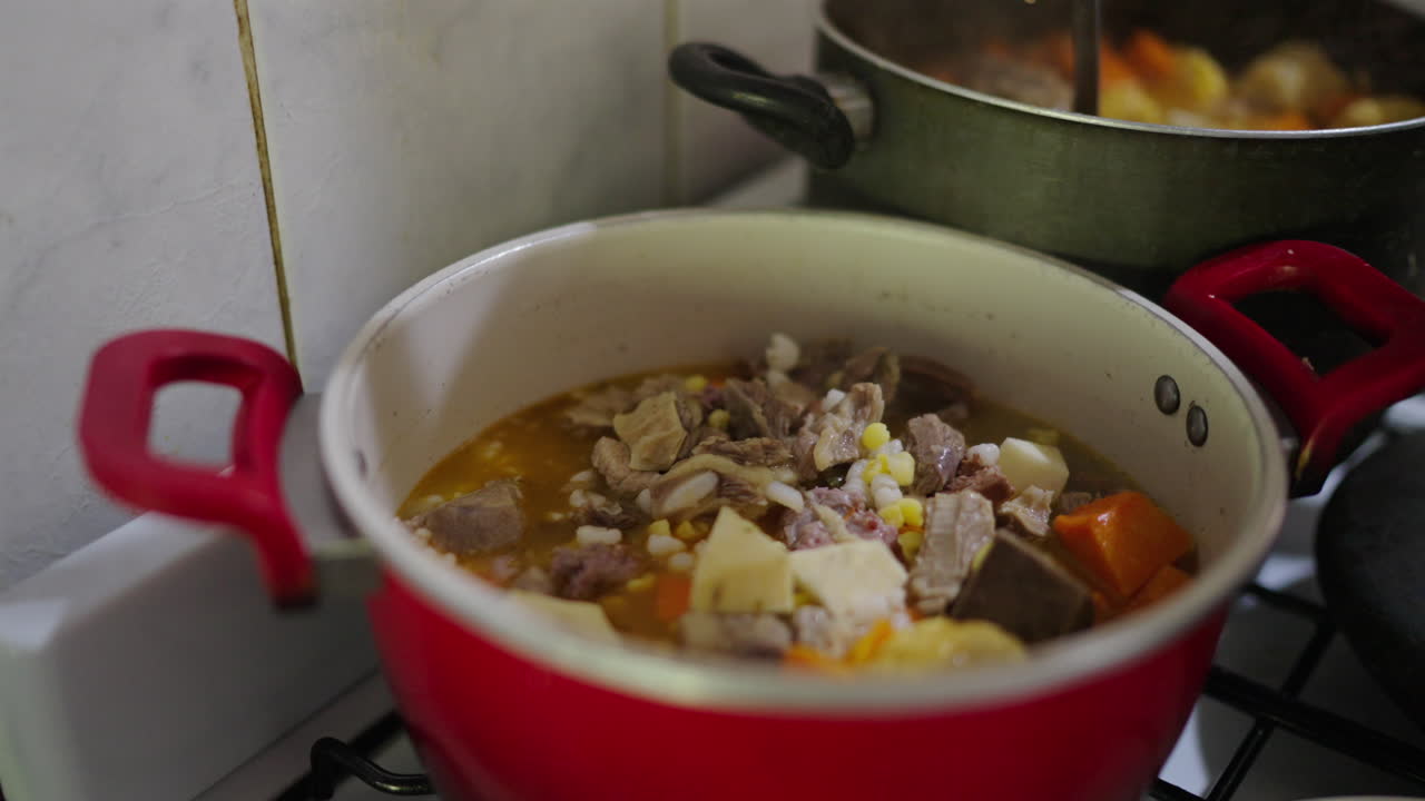 Thick Argentinian stew with corn kernels cooking in red pot on stove, traditional dish, detailed sideview