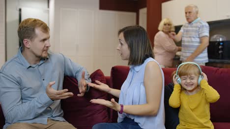 family in living room - a young girl is listening to music with headphones while her parents argue on the couch.