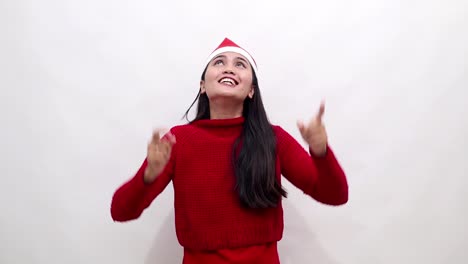 cheerful young asian woman wear warm red sweater and xmas santa hat point index finger overhead indicate on workspace area