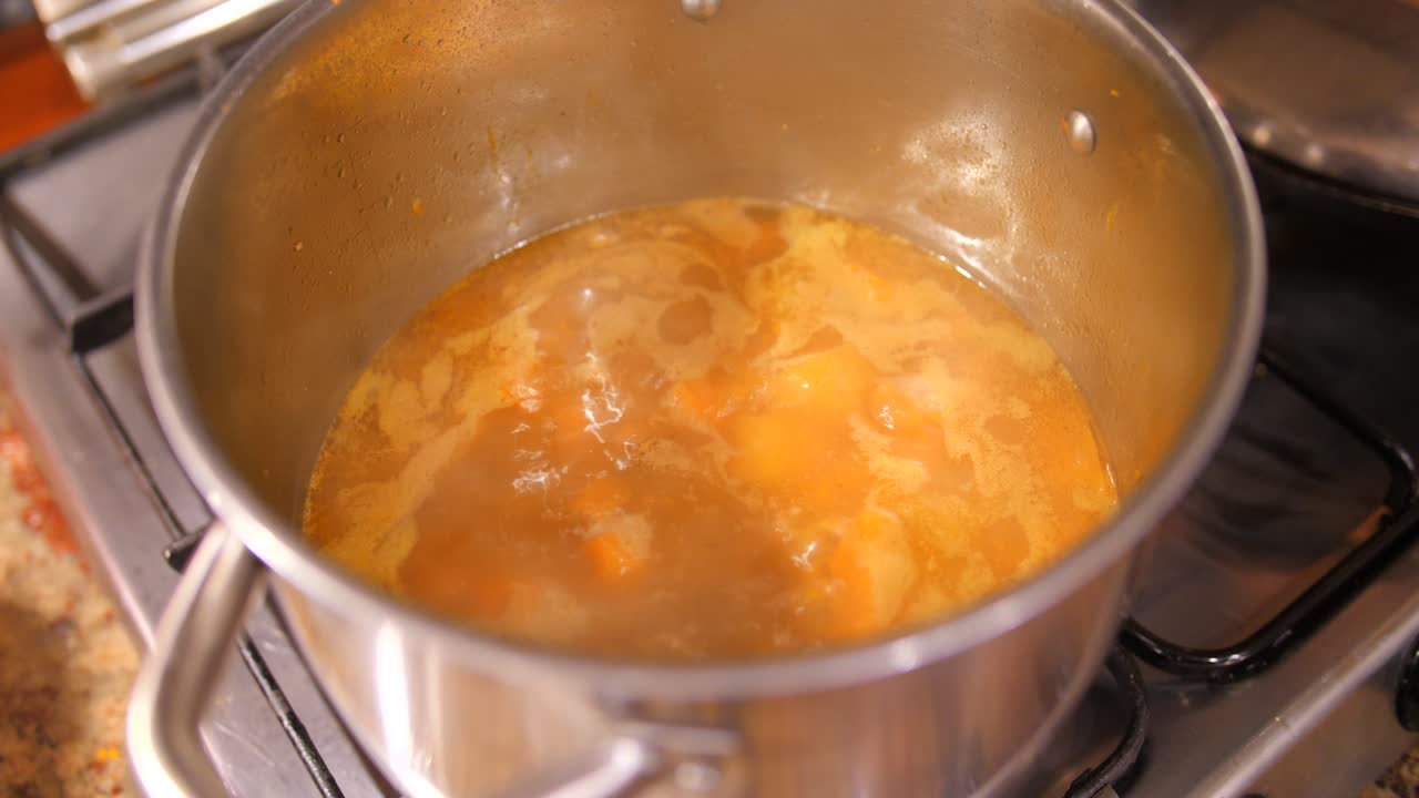 Overview of Delicious butternut squash soup simmering in a stockpot over the gas in the kitchen