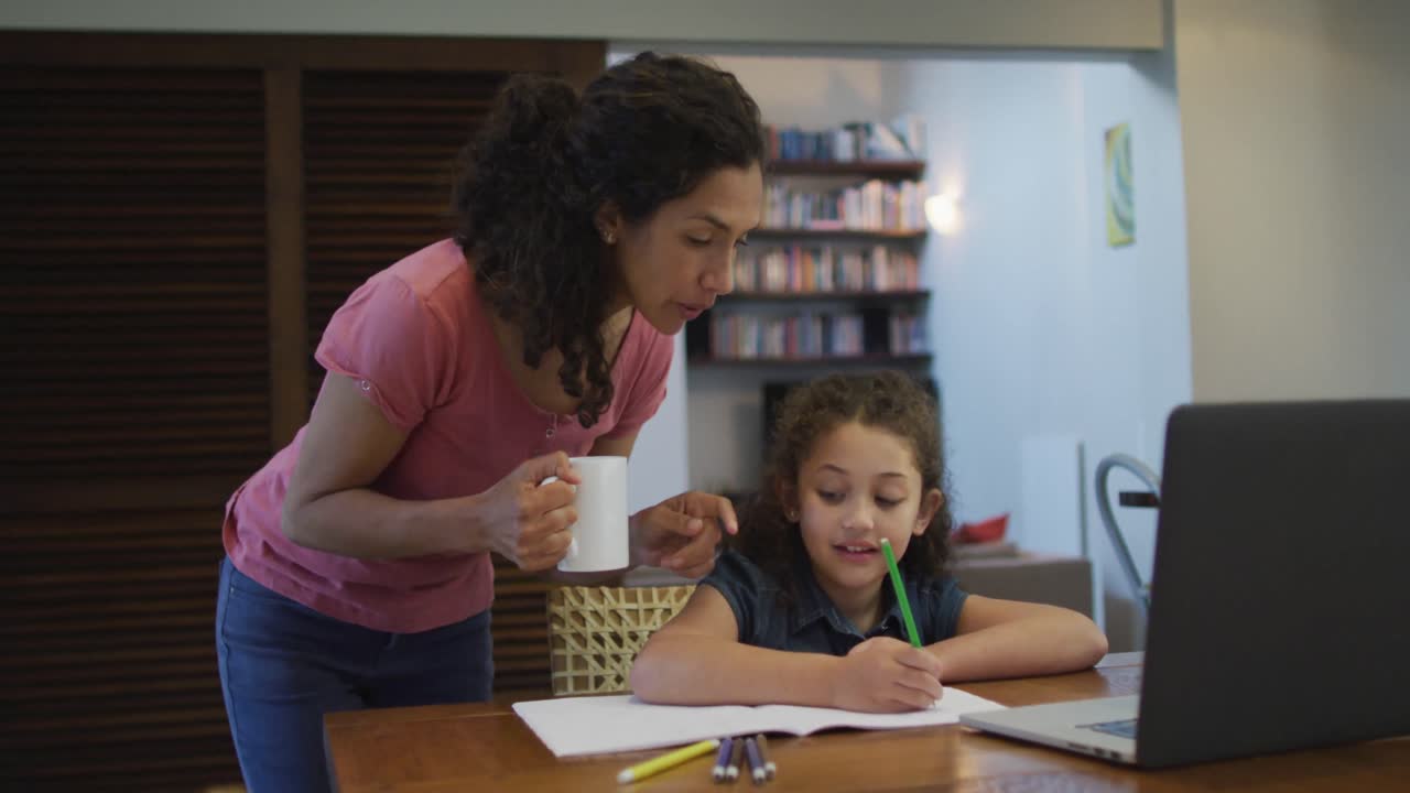 madre e hija de raza mixta felices haciendo la tarea juntos en casa