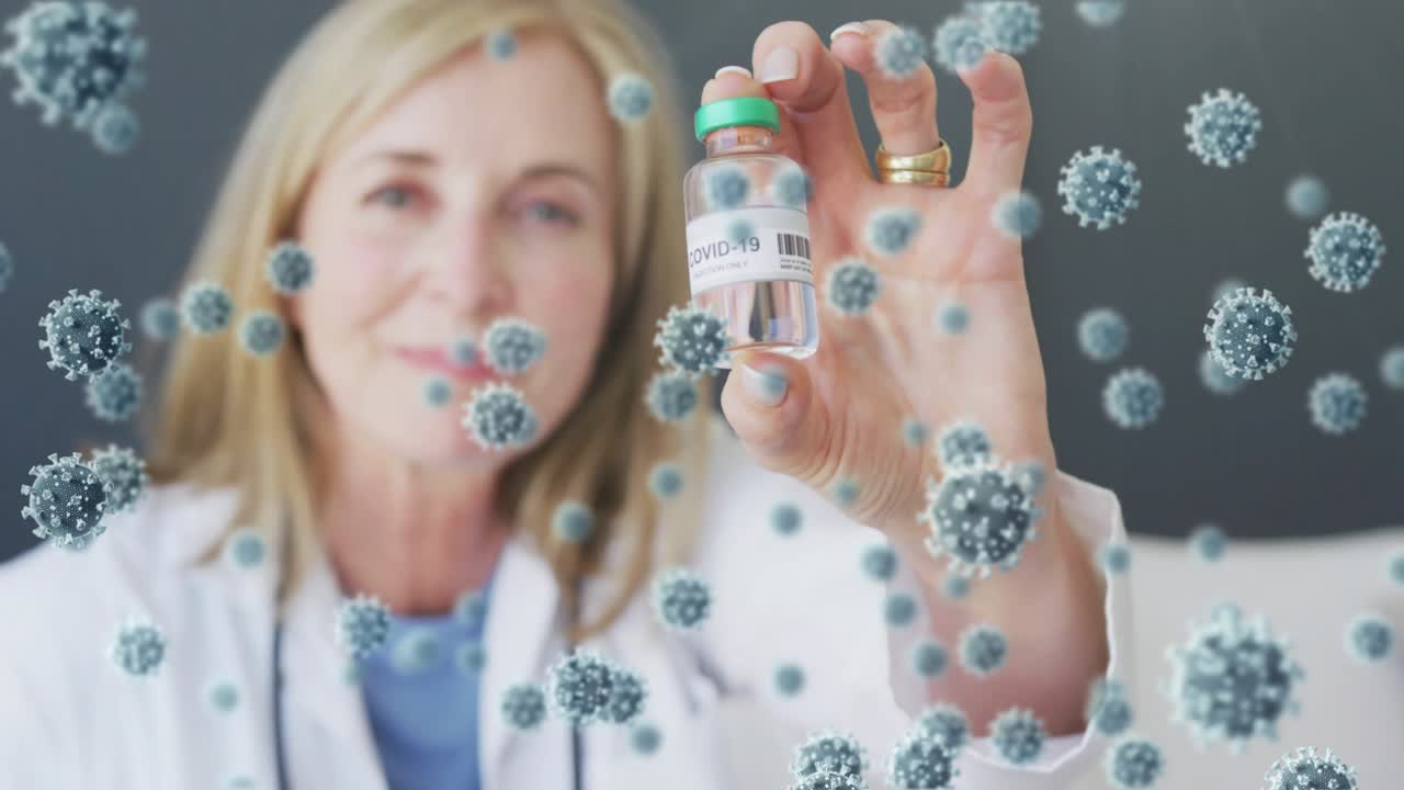 Female doctor lifting COVID-19 vial forward in clinic, showing label while virus particles floating