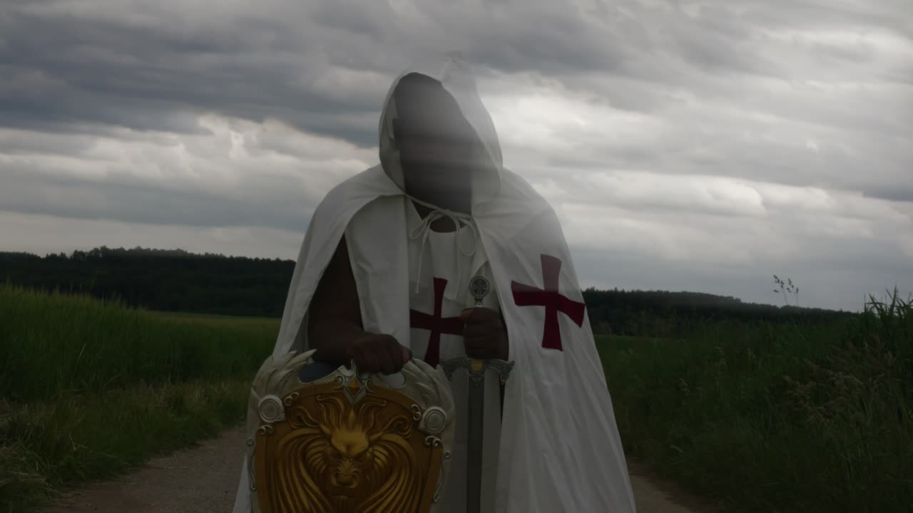 Angelo guerriero maschio nero con nuvole che si muovono sul viso, inginocchiato nel campo in abiti da Cavaliere Templare, con il tempo che scorre velocemente sullo sfondo, timelapse, Stoccarda, Germania, Baviera, Baden-Württemberg, Europa
