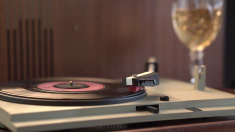 comenzando a tocar discos de vinilo en un gramófono vintage de los años 70 con un vaso de vino en el fondo