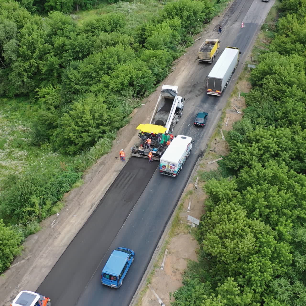 Roadworks on the highway. Trucks and cars passing near the road construction site in summer. Aerial view. Camera moves top down.