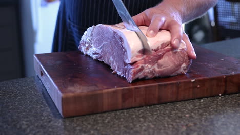 a man cutting a fresh meat on the wooden board using a knife - close up shot