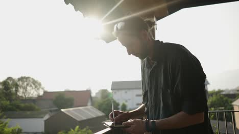 man working on a tablet with a stylus on a sunny balcony
