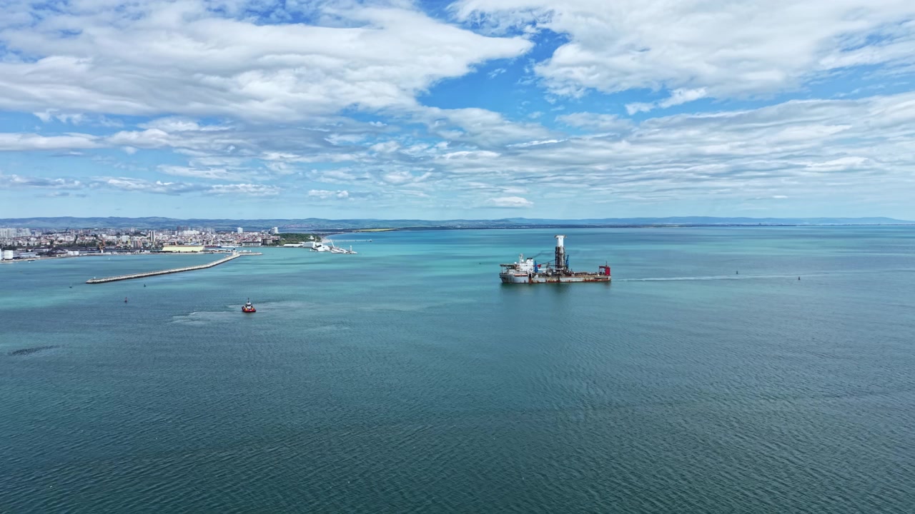 Industrial dredging vessel working near the shoreline with city skyline in the background and ships in the water during a clear day