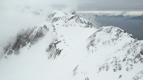 Aufschlussreiche-Drohnenaufnahme-Eines-Paares,-Das-Auf-Dem-Gipfel-über-Der-Schneebedeckten-Alpenlandschaft-Steht