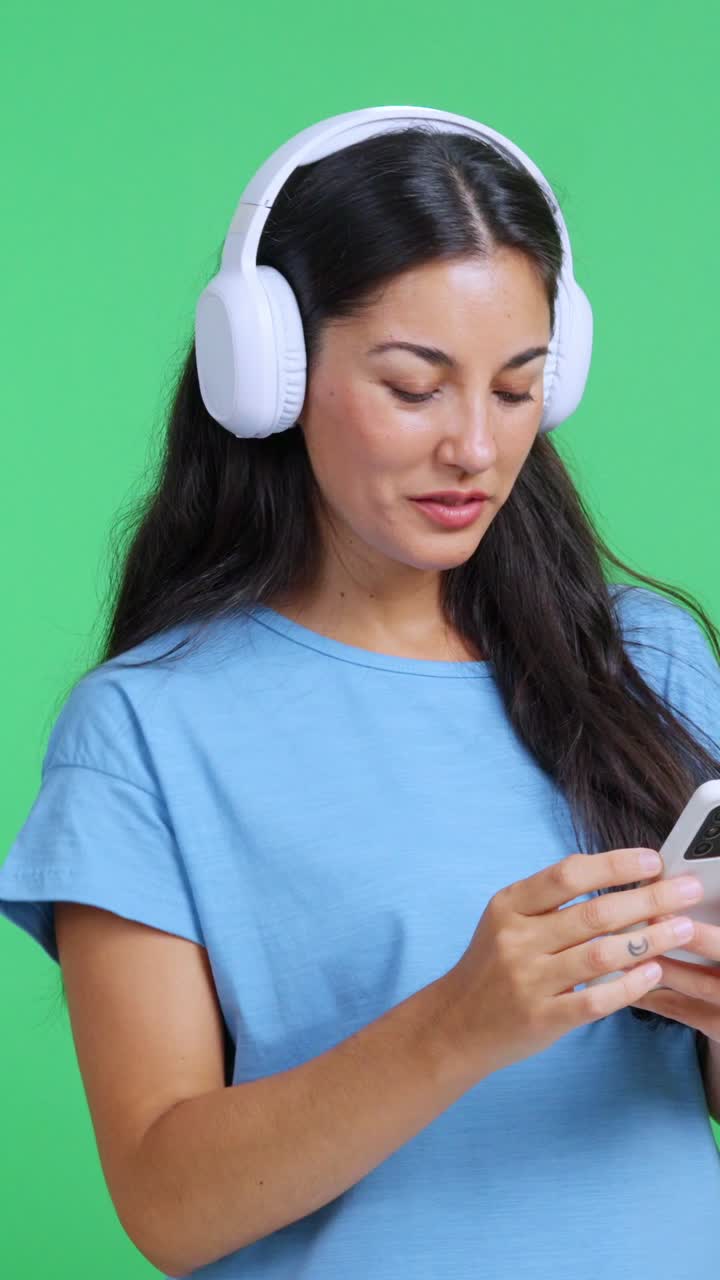 Giovane donna che indossa le cuffie e balla con uno smartphone.