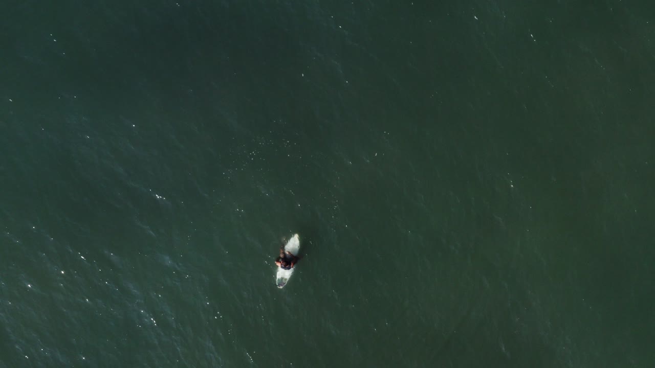 surfista sentado y relajado en la tabla de surf en el océano, vista aérea de arriba hacia abajo