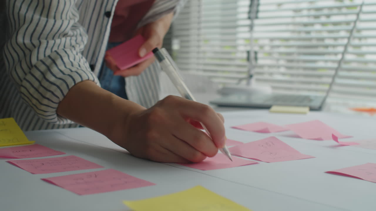 Project Manager Writing Ideas on Stickers when Working on Project