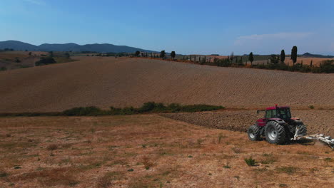 Male-farmer-driving-a-tractor-in-the-fields-to-remove-all-grass-and-make-land-ready-for-agriculture-in-wineyard-of-Tuscany,-Italy-during-day