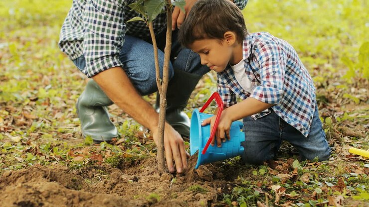 Closeup. Portrait of a little boy and his dad planting a tree. The boy puts the soil onto the roots. Dad presses the soil. The son helps him with his spade. Blurred background
