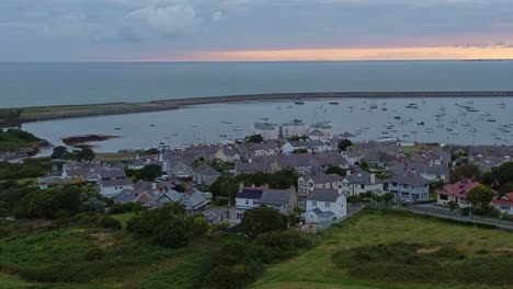 Drone panning over Penrhos reveals grassy hills, houses, a bay filled with boats, and the warm glow of a sunset sky