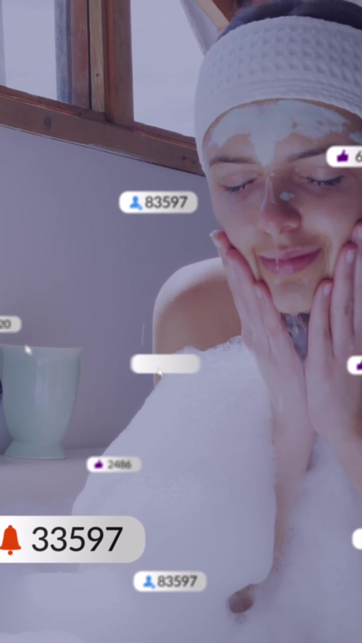 Giovane donna che si lava il viso nella vasca da bagno con schiuma e maschera facciale