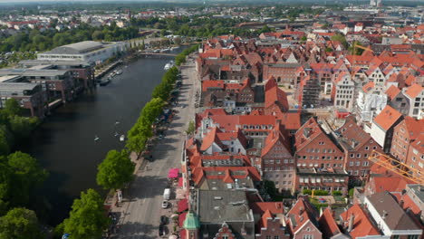 Aerial-sliding-footage-of-historic-brick-town-houses,-wide-riverside-street-and-Trave-river.-Luebeck,-Schleswig-Holstein,-Germany