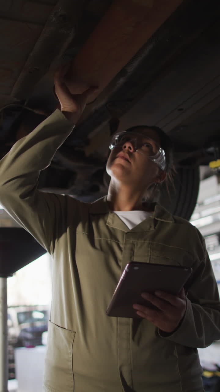 video vertical de una mecánica de automóviles biracial usando una tableta y comprobando el coche