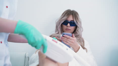 woman-in-goggles-with-cellphone-undergoes-laser-epilation