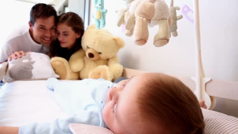 Happy-parents-watching-over-baby-son-in-crib-