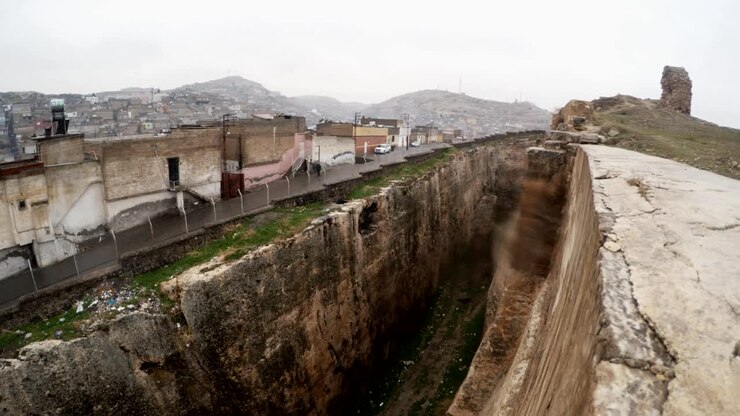 Fossato scavato a mano del Castello di Urfa che divide rovine e baraccopoli sotto la neve e la pioggia