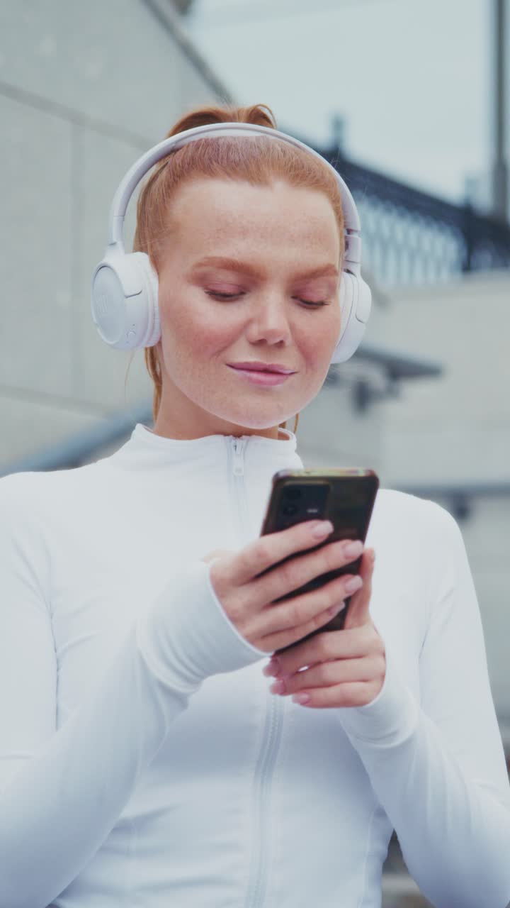 A Confident Young Woman Enjoying Music on Her Headphones While Checking Her Phone, Exuding Focus and Joy in a Modern Urban Setting