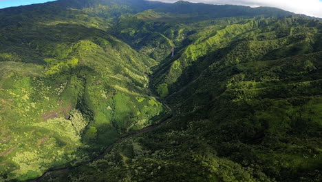 vista aérea de colinas onduladas y paisaje verde con cascada en la distancia en kauai hawaii