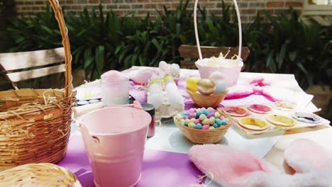 table in garden with bunny ears, baskets, painted and sugar eggs for easter celebration, slow motion