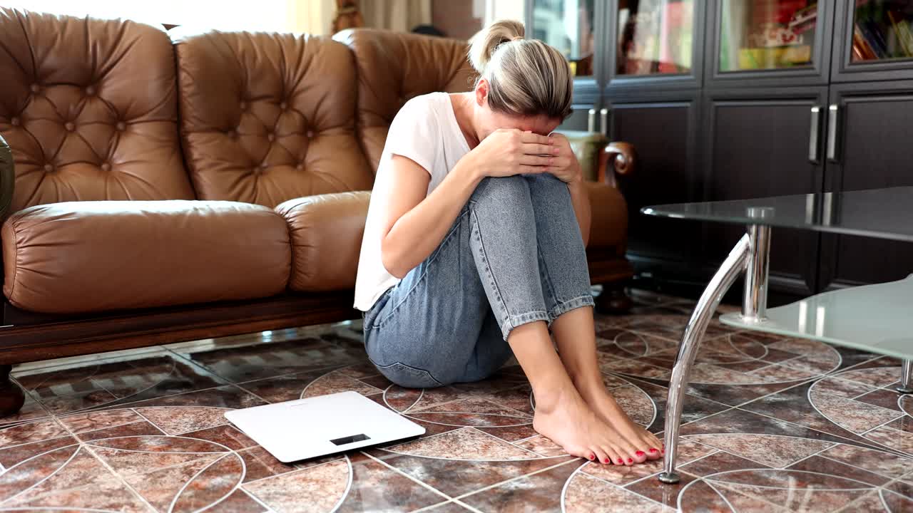 Donna triste seduta sul pavimento con bilancia