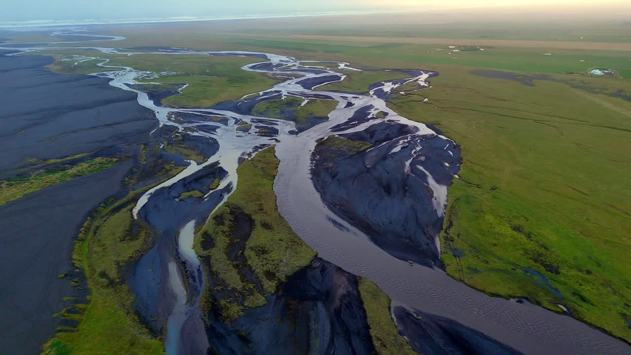 Icelandic streams twist like veins on their journet through glaciated valleys, volcanic rock and vibrant mossy green flatlands to the sea. Drone aerial reveal horizon