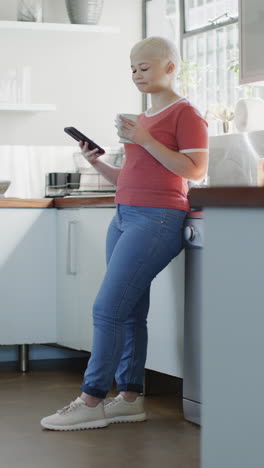 vertical video of happy biracial woman using smartphone and drinking coffee in slow motion