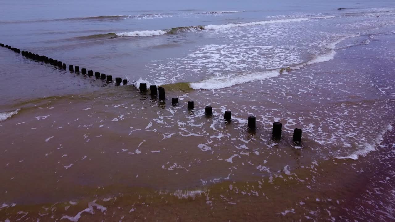 hermosa vista aérea de un viejo muelle de madera en la costa del mar báltico, día nublado, playa de arena blanca afectada por la erosión costera del mar, costa tranquila, tiro de drones de ojo de pájaro de gran angular que avanza