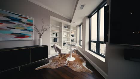 wide push in shot of a reading nook with large white shelving, white chairs, and a white table, next to large windows letting in natural sunlight