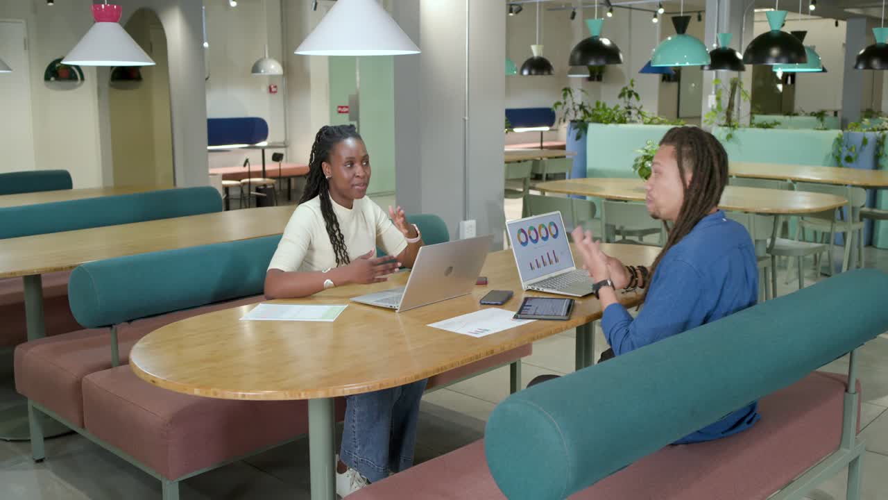 African American coworkers turning laptop showing chart, cheering win and planning steps at office