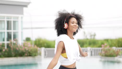 african woman in sportswear wearing headphones dancing at swimming pool background .