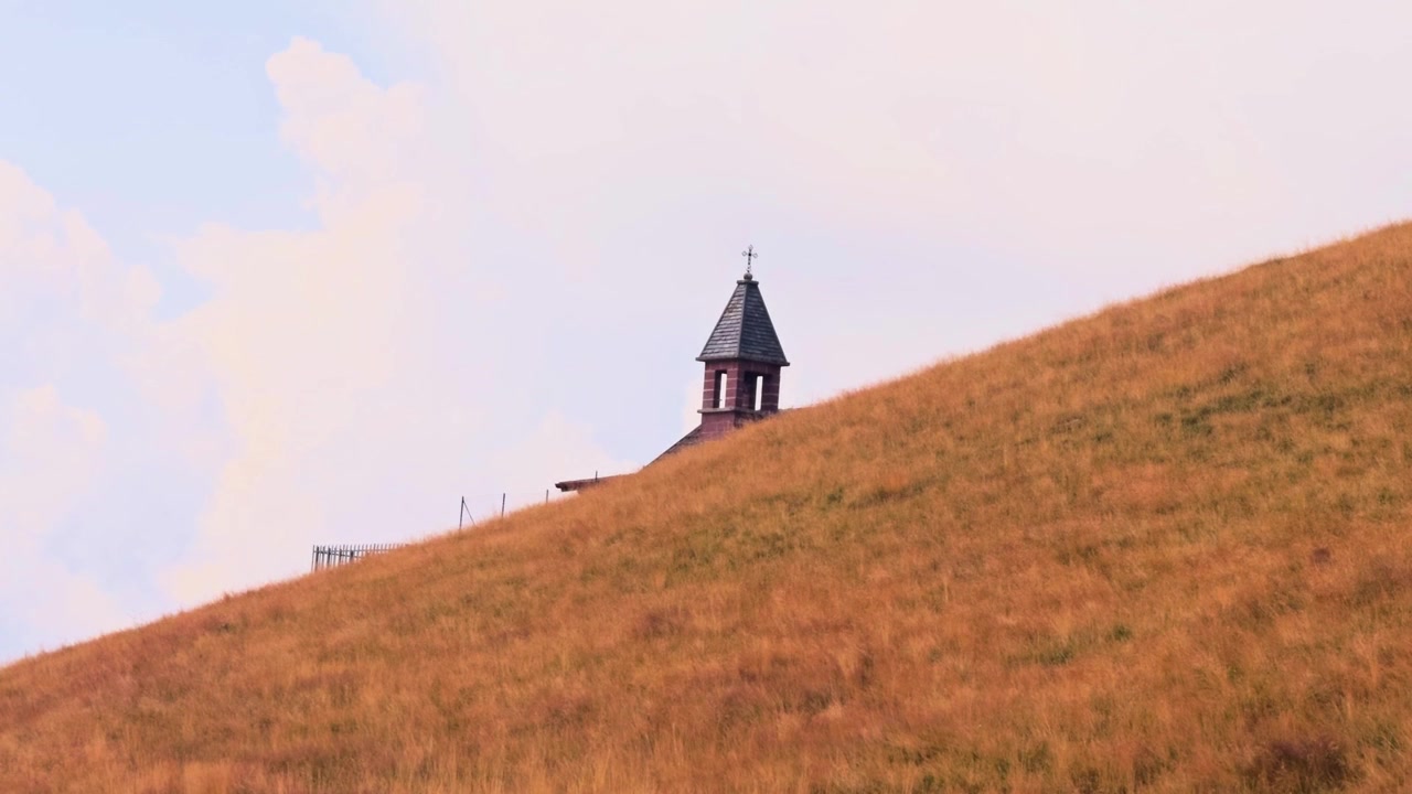 Lonely christian chapel with a bell tower standing on a grassy, golden hillside. This serene and peaceful mountain landscape is in colonno, italy