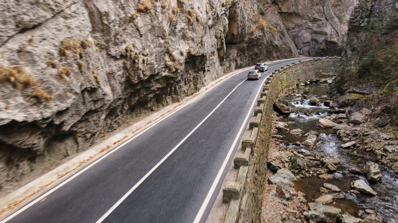 Aerial drone view of nature in Romania. Carpathian mountains, road with cars in the valley, rocky cliffs, river