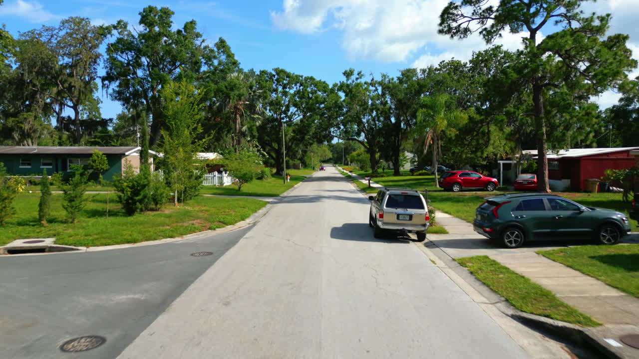 Drone forward motion above empty Tampa suburban street with tree shadows under clear blue summer sky