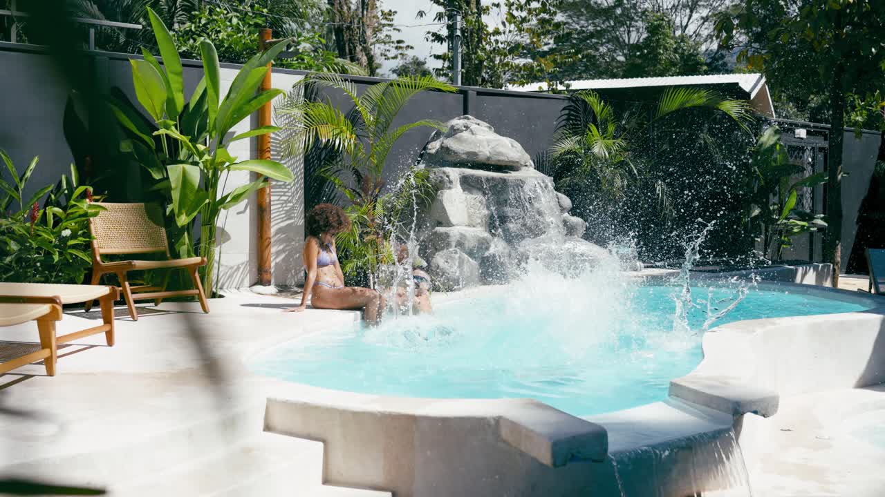 Kvinde hopper i swimmingpoolen med venner på et tropisk resort