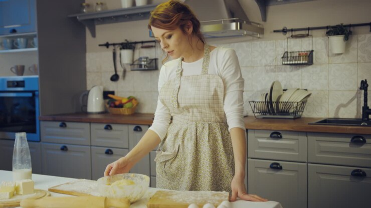 Portrait shot of the young charming woman in the apron and with a flour on her face making a daugh and smiling to the camera in the kitchen. Indoor