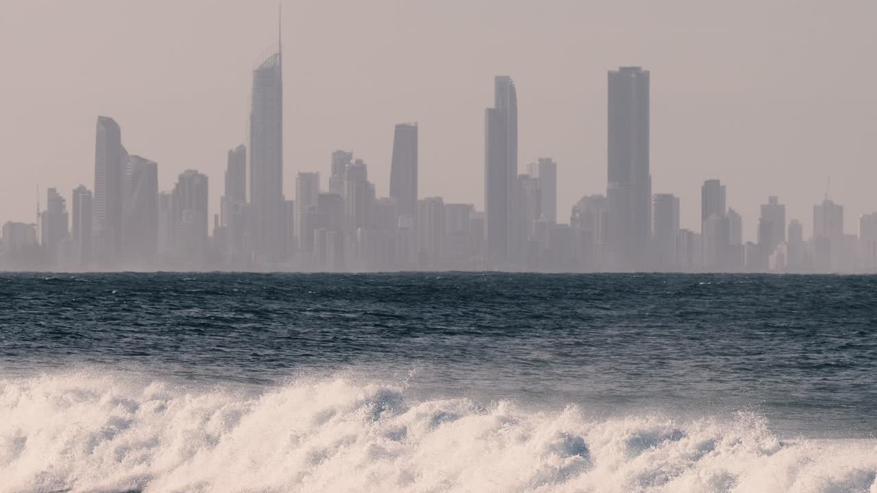 서퍼 는 멀리 떨어진 도시 스카이 라인 근처 에서 파도 를 타고 있다