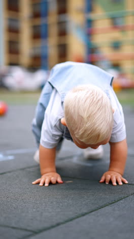 funny blond toddler boy stands on all fours at the playground. cute kid stands up and runs away. vertical video.